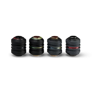 May include: Four black bottle stoppers with a textured, ribbed design. Each stopper has a gold-colored base and a decorative band in red, green, or blue. The tops are also accented with gold and red.
