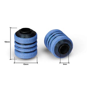 Könnte beinhalten: Zwei blau-schwarze Spulen, jeweils etwa 1,8 cm hoch, 1,5 cm breit und 0,6 cm dick. Die Spulen haben eine zylindrische Form mit schwarzer Ober- und Unterseite und blauem Faden, der um die Mitte gewickelt ist.