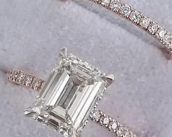 May include: Two rings in a light blue ring box. The primary ring features a large, emerald-cut diamond. The band is adorned with small, sparkling stones. A second, thinner band with small stones is also present, creating a set.