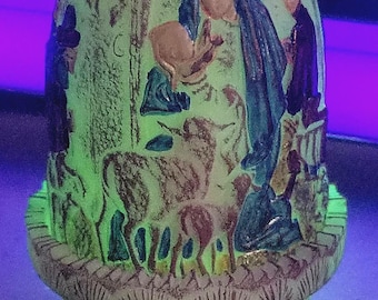 May include: An egg-shaped, off-white ceramic decorative piece with a religious scene. The piece features a depiction of the Virgin Mary in blue, holding a baby, with other figures and animals. The base has a detailed, textured design.