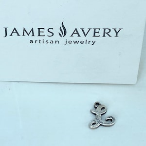 May include: A silver-colored charm in the shape of the letter "L" sits in front of a white background. The charm is from James Avery Artisan Jewelry. The brand's logo is printed in black above the charm.