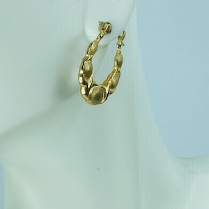 May include: A close-up of a gold-colored hoop earring. The earring has a textured, twisted design with rounded, bead-like accents. The earring is displayed against a white background.