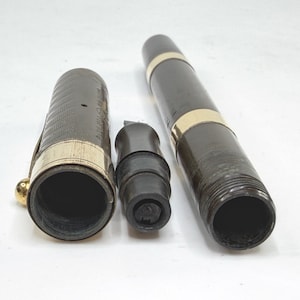 May include: A disassembled fountain pen with a dark brown barrel and cap, accented with gold-colored bands. The pen's nib section is black. The cap has a gold-colored clip and a textured pattern. The pen is lying on a white surface.