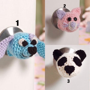 May include: Three crocheted animal door knob covers. The first is a blue dog with purple ears, the second is a pink cat with purple ears and nose, and the third is a black and white panda.