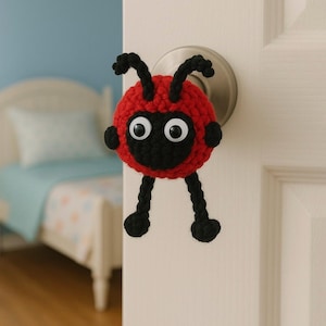 May include: A handmade, red and black crocheted ladybug door knob cover with googly eyes. The ladybug has black antennae and legs, adding a whimsical touch to a child's bedroom door. The door knob is silver.