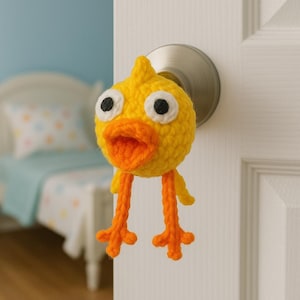 May include: A handmade yellow crochet chick with orange beak and legs, attached to a door handle. The chick has large black and white eyes and an open beak. The crochet chick is a whimsical decorative item.