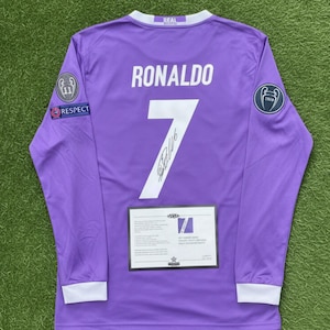 May include: A long-sleeved purple football shirt with the name "RONALDO" and the number "7" in white. The shirt has white cuffs and patches on the sleeves. A certificate is displayed below the number.