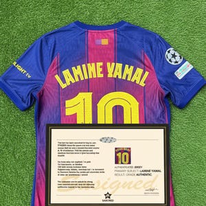 May include: A blue and maroon soccer jersey with the name "LAMINE YAMAL" and the number "10" in yellow. The jersey is displayed on a green surface, with a framed certificate below it. The certificate reads "AUTHENTICATED JERSEY".