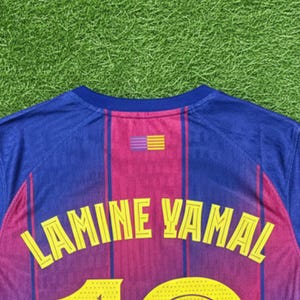 May include: A blue and maroon soccer jersey with the name "LAMINE YAMAL" in yellow lettering across the back. The number "10" is also visible in yellow. The jersey has a striped design and a small emblem.