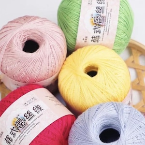 Puede incluir: Una colección de madejas de hilo coloridas en tonos rosa, verde, amarillo, rojo y azul. Cada madeja está cuidadosamente enrollada, con etiquetas visibles en algunas. El hilo parece suave y adecuado para proyectos de tejido o ganchillo.