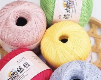 May include: A collection of colorful yarn skeins in shades of pink, green, yellow, red, and blue. Each skein is neatly wound, with labels visible on some. The yarn appears soft and suitable for knitting or crochet projects.