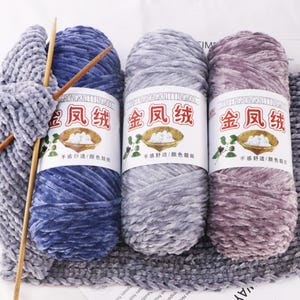 May include: Three spools of soft velvet yarn in blue, grey, and mauve, with labels featuring Chinese characters and illustrations. Knitting needles and a knitted swatch are also visible, suggesting a crafting project.