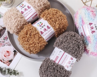 May include: A collection of teddy perm knitting yarn in various colors, including beige, brown, and gray. The yarn is arranged on a gray plate. Each skein has a label with Chinese characters and the words "Teddy perm KNITTING".