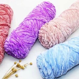 K&ouml;nnte beinhalten: Nahaufnahme von vier Kn&auml;ueln weicher, pl&uuml;schiger Wolle in Rot-, Lila-, Rosa- und Blaut&ouml;nen. Das Garn hat eine samtige Textur, perfekt f&uuml;r Strick- oder H&auml;kelprojekte. Einige Zweige getrockneter Blumen befinden sich im Vordergrund.