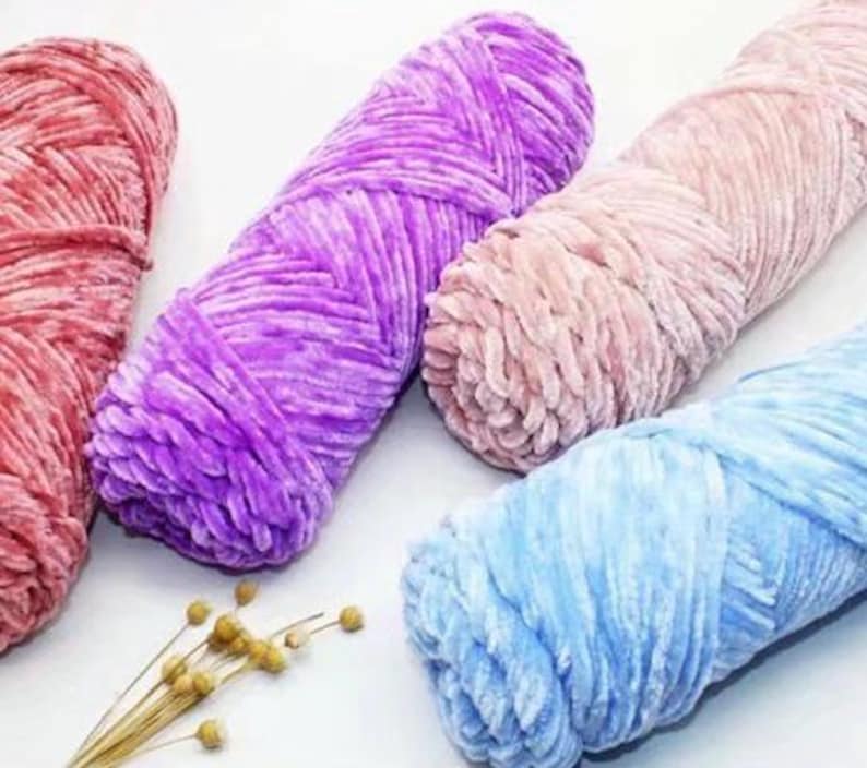 K&ouml;nnte beinhalten: Nahaufnahme von vier Kn&auml;ueln weicher, pl&uuml;schiger Wolle in Rot-, Lila-, Rosa- und Blaut&ouml;nen. Das Garn hat eine samtige Textur, perfekt f&uuml;r Strick- oder H&auml;kelprojekte. Einige Zweige getrockneter Blumen befinden sich im Vordergrund.