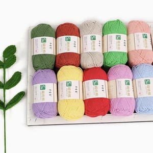 May include: A selection of colourful yarn skeins in shades of green, red, yellow, and pink. Each skein is labelled with text in a foreign language. The yarn is neatly arranged, suggesting a craft or knitting project.