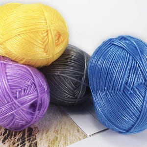 May include: Four balls of yarn in yellow, purple, grey, and blue. The yarn is tightly wound, displaying the texture and colour variations. Suitable for knitting, crochet, or other yarn crafts. Each ball is approximately 100g.