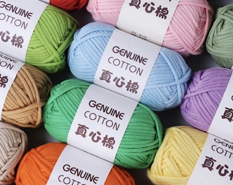 May include: A collection of colorful yarn skeins in various shades, including red, pink, green, blue, and orange. Each skein is labeled with "GENUINE COTTON" and Chinese characters. The yarn is tightly wound, suggesting it's ready for crafting projects.