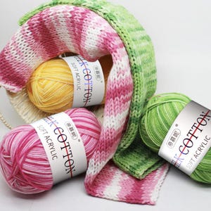 May include: A collection of colorful yarn and knitted fabric. The yarn is in shades of yellow, pink, and green, with labels that read "LK COTTON SOFT ACRYLIC". The knitted pieces display pink and white stripes and green and white stripes.