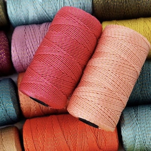 Könnte beinhalten: Nahaufnahme von farbenfrohen Garnrollen in Rosa-, Orange-, Türkis- und Goldtönen. Der Faden ist eng gewickelt und die Rollen sind in einem optisch ansprechenden Muster angeordnet. Das Bild zeigt eine Vielzahl von Farben und Texturen, ideal für Bastelprojekte.