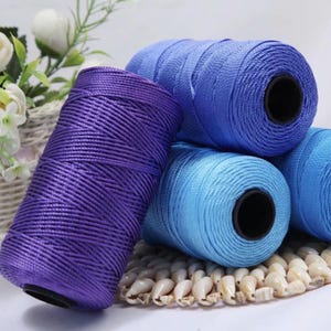 Puede incluir: Carretes de hilo de nailon de colores en tonos morado, azul y azul claro. Los carretes están bien enrollados y tienen un brillo brillante. Estos hilos son adecuados para diversos proyectos de manualidades, como macramé y bisutería.