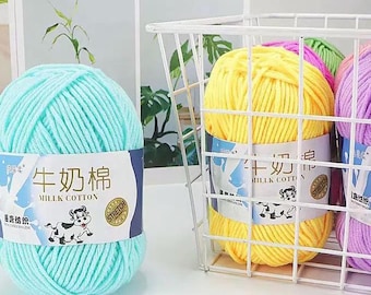 Può includere: Primo piano di gomitoli di filato in vari colori, tra cui azzurro, giallo e viola. Il filato è etichettato "Milk Cotton" con una grafica di una mucca. Il filato è in un cestino di filo bianco.
