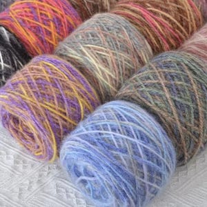 May include: Close-up of several skeins of colorful yarn. The yarn is a mix of colors, including purple, yellow, orange, blue, and brown. The yarn is soft and fluffy, perfect for knitting or crocheting projects.