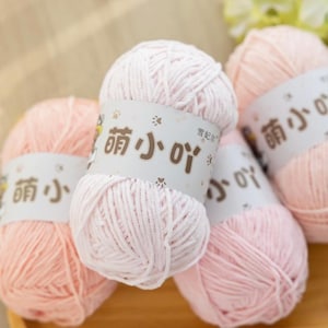May include: A collection of light pink yarn balls, each with a label featuring Chinese characters and paw prints. The yarn has a soft, fluffy texture, ideal for knitting or crochet. The image suggests a craft or hobby theme.