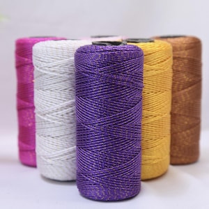 May include: A selection of colourful thread spools, tightly wound. The threads are in shades of pink, white, purple, gold, and brown. The thread has a metallic sheen, adding a touch of sparkle. Suitable for crafting and sewing projects.
