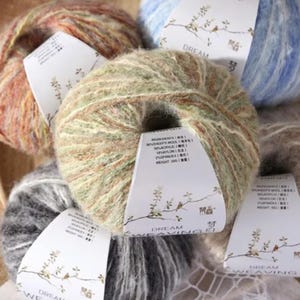 May include: A selection of colourful yarn skeins, including shades of green, brown, and blue. Each ball has a label with the text "DREAM WEAVING" and ingredient details. The yarn looks soft and fluffy, ideal for knitting or crochet.