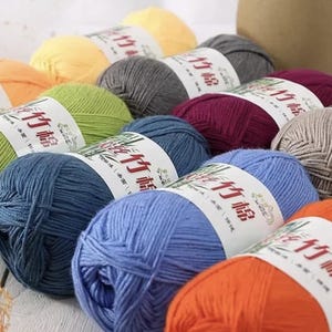 May include: A selection of colourful yarn balls in shades of yellow, green, grey, blue, orange, and burgundy. Each ball has a white label with Asian characters. The yarn is likely for knitting or crocheting projects.