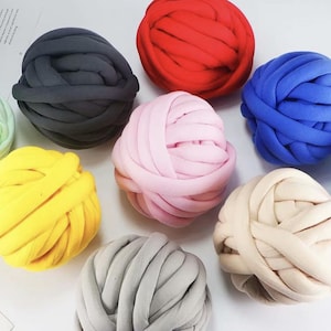 May include: A selection of large, colourful yarn balls in various shades. The yarn balls are in shades of red, blue, pink, yellow, grey, and black. The yarn appears to be a thick, chunky knit, suitable for crafting projects.