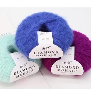 May include: Three balls of Diamond Mohair yarn in blue, purple, and mint green. Each ball has a white label with the brand name and logo. The yarn is soft and fluffy, suitable for knitting or crochet projects. The labels include Chinese text.