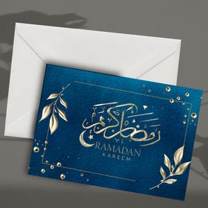 May include: A blue Ramadan greeting card with gold calligraphy and the words "Ramadan Kareem." The card features gold leaf accents and a gold border. A white envelope is behind the card.