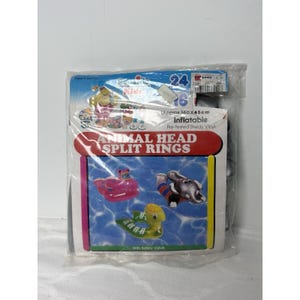 May include: A clear plastic package containing an inflatable animal head split ring. The packaging features the text ANIMAL HEAD SPLIT RINGS, illustrations of a pink, gray, and green animal-shaped pool float, and states Approx 63 x 18 inches.