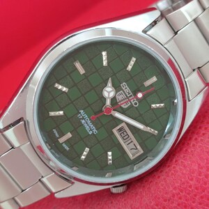 May include: A silver-tone stainless steel Seiko 5 automatic wristwatch featuring a dark green checkered dial, silver hour markers, luminous hands, a red second hand, and a day-date window at the three o'clock position with the text WED 17.