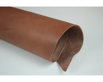 Puede incluir: Un rollo de cuero marrón, que muestra una superficie lisa y texturizada. El cuero tiene un tono cálido y terroso, con grano visible y ligeras variaciones de color. Los bordes del rollo revelan el grosor y la textura del material.