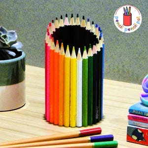 Könnte beinhalten: Ein zylindrischer Stifthalter aus farbigen Bleistiften. Die Bleistifte sind vertikal angeordnet und erzeugen einen Regenbogeneffekt. Der Stifthalter hat ein schwarzes Innenleben und die Worte "pencil pot" sind in einem Kreis rechts oben.