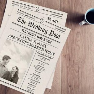 Op de afbeelding: Twee kranten met de titel "The Wedding Post" met de kop "De mooiste dag ooit, Laura & Joey gaan vandaag trouwen". Een foto van een stel staat in het midden. Een blauwe mok staat op een houten oppervlak.