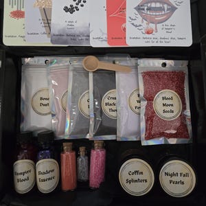 Peut inclure: Un ensemble d'ingrédients de potions et de cartes de sorts. L'ensemble comprend de petites bouteilles en verre étiquetées "Vampire Blood" et "Shadow Essence", des sachets de poudres et des cartes avec des incantations. Une cuillère en bois repose dessus.
