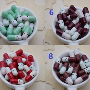 Puede incluir: Una colecci&oacute;n de cuentas coloridas en forma de c&aacute;psula sonriente en un cuenco de cer&aacute;mica blanco. Las cuentas est&aacute;n en varias combinaciones de colores, incluyendo verde y blanco, burdeos y blanco, y rojo y blanco. Cada cuenta tiene una cara sonriente.