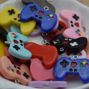 May include: A collection of colourful plastic game controller charms with different coloured buttons and a heart design. The charms have a silver loop for attaching to a keychain or bracelet.