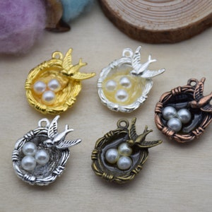 May include: Five silver and gold bird nest charms with pearl-like eggs. Each charm features a bird with outstretched wings.