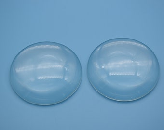 May include: Two clear glass dome lenses on a light blue background.