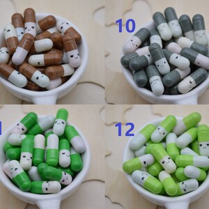 Puede incluir: Una colecci&oacute;n de objetos caprichosos con forma de c&aacute;psula sonriente en varios colores, incluyendo marr&oacute;n, gris, verde y blanco. Cada c&aacute;psula tiene una cara linda dibujada. Las c&aacute;psulas est&aacute;n dispuestas en peque&ntilde;os cuencos blancos.