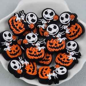 May include: A collection of small, flat, rubberised charms featuring a white skeletal character with a wide grin and a small white ghost dog sitting atop a bright orange jack-o'-lantern with black carved facial features and accents.