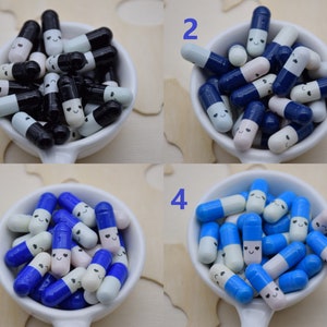 Puede incluir: Una colecci&oacute;n de cuentas decorativas en forma de c&aacute;psula en un cuenco blanco. Las cuentas est&aacute;n en cuatro combinaciones de colores: negro y blanco, azul marino y blanco, azul y blanco y azul claro y blanco. Cada cuenta tiene una cara sonriente.