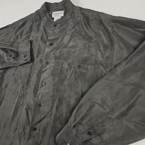May include: A dark gray button-down shirt with long sleeves and two chest pockets. The shirt has a mandarin collar and the brand name "MONTAGE" is visible on the label.