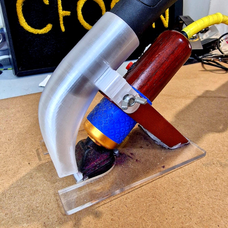 May include: A custom-built tool featuring a clear plastic guide, a silver metal clamp, and a wooden handle. The tool has a blue and gold cylindrical component and a black head. A yellow cable extends from the top.