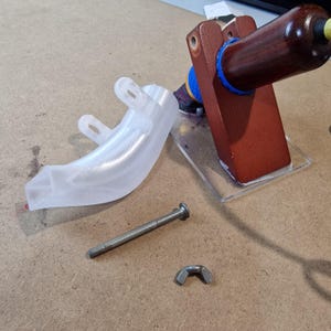 May include: A disassembled wooden stamp with a clear plastic base, a clear plastic curved piece, a bolt, and a wing nut. The stamp has a dark brown handle and a blue ring.